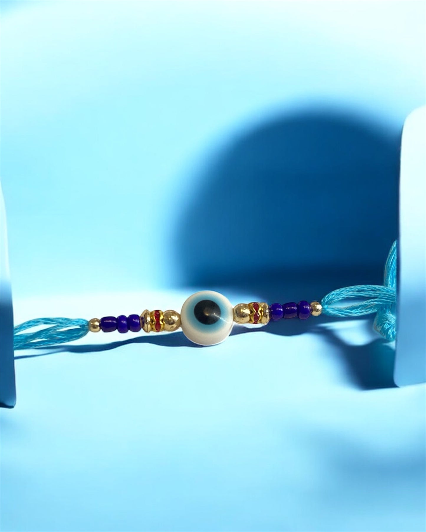 White Evil Eye Rakhi with Light Blue Thread & Gold Beads – Rakhi for Brother | Handmade Rakhi UK